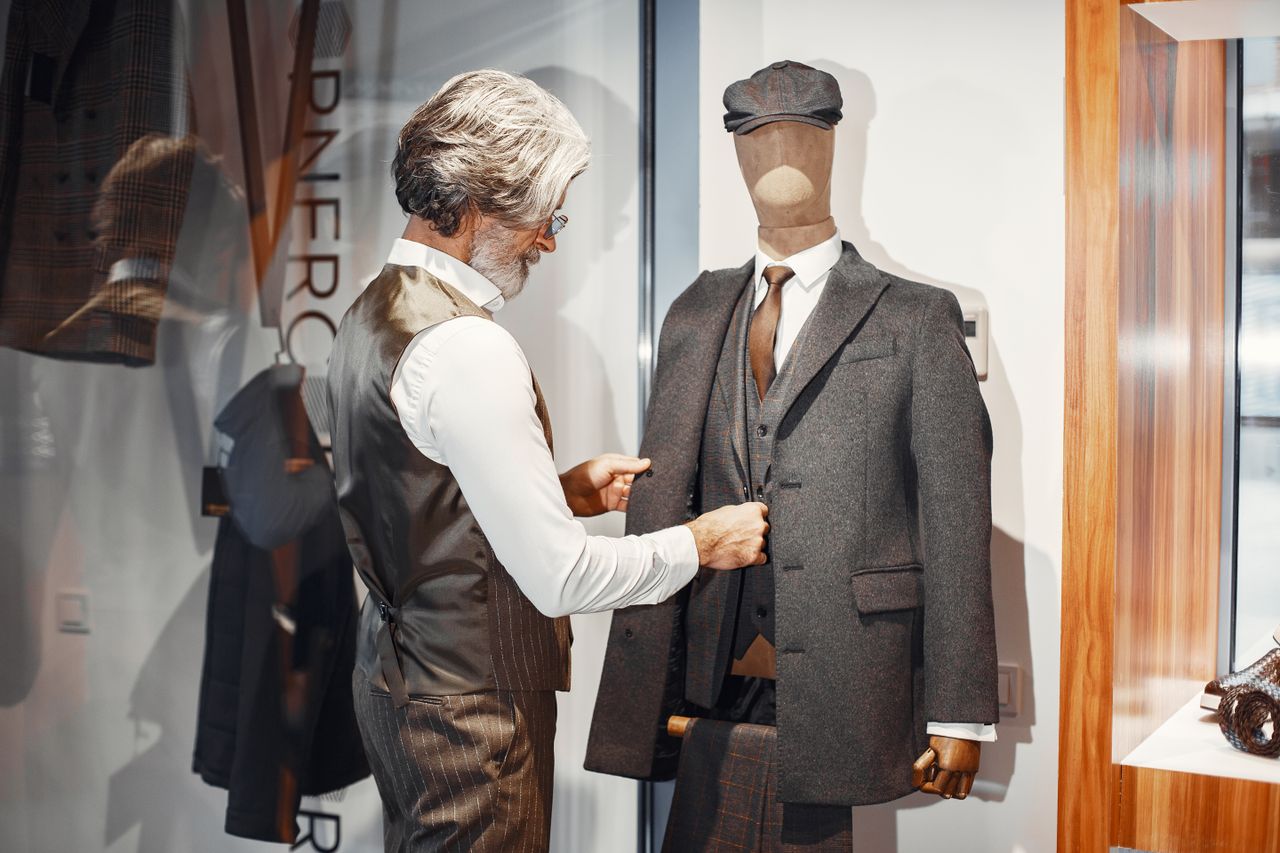 Mastering the First Impression: Your intriguing post title goes here Man adjusting a tailored suit on a mannequin in a formal wear store, highlighting fashion elegance and craftsmanship.
