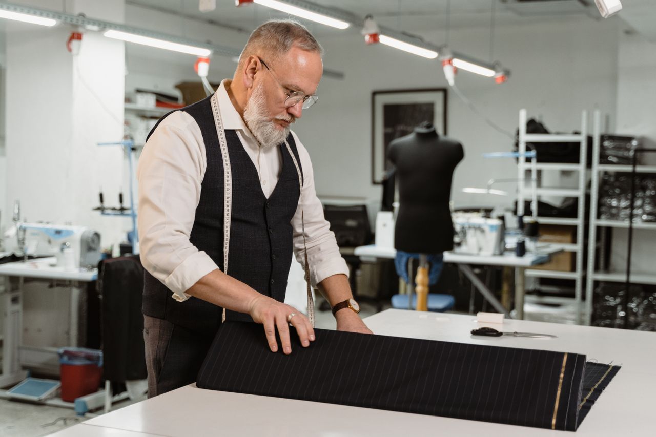 About An experienced tailor focusing on fabric for a custom suit in his workshop.